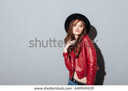 Picture of young pretty woman standing over grey wall wearing hat. Looking at camera.