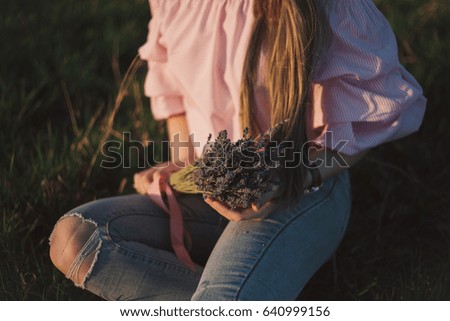 Beautiful young woman sitting in a meadow with a bouquet of lavender and dreaming in the sunset rays