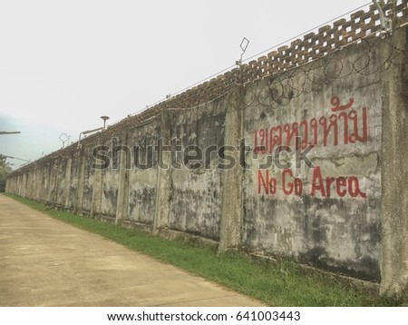 Prison wall, view of old raw concrete prison wall with "No Go Area" in English and Thai letters sign