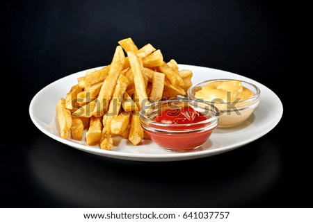 Crispy french fries on the plate with catchup and cheese sauce isolated on black background