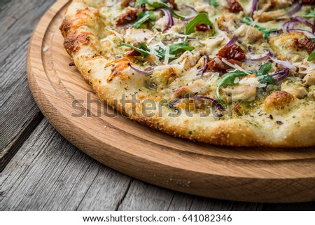 pizza with sun-dried tomatoes, prosciutto, arugula and parmesan cheese on a plate on the table