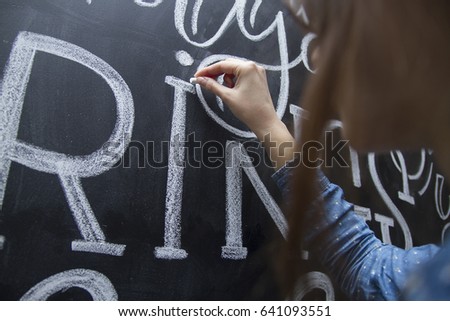 Young woman writing lettering on the chalkboard using chalk