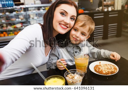 A young mother makes selfie with her little cute son at a table in a cafe