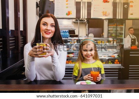 young mother with her little cute dauther sitting at a table in a cafe and drinking juice