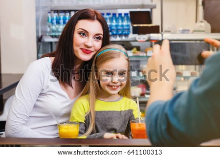 A man makes picture of young mother with her little cute dauther at a table in a cafe