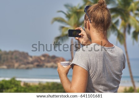 Self portrait of the photographer taking a picture of a beach while holding a coffee cup.