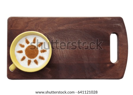 A cute yellow cup with coffee cream. Food art creative concept image, Sun shape drawing with cinnamon powder over wooden cutting board background.