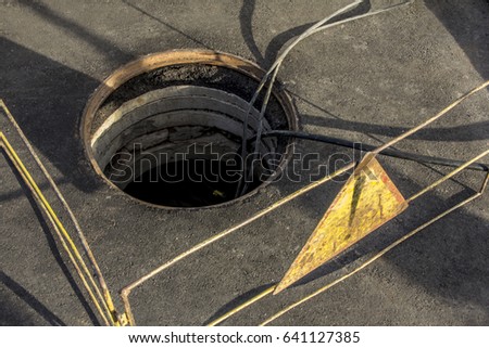 cable layout into a sewer well on the asphalted road enclosured by railings showing attention sign