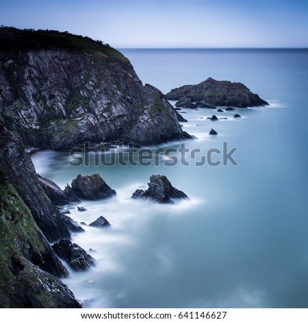A long exposure of a rocky headland and blue sea in Wales