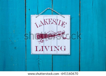 Lakeside Living sign with red fishing rowboat hanging on antique rustic teal blue wood background; wooden beach holiday vacation sign with painted copy space