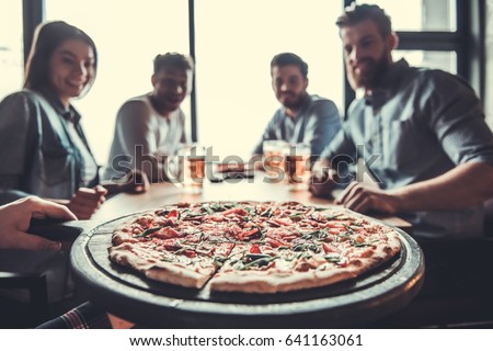 Pizza time. Close-up of tasty pizza on the table, with a group of young smiling people resting in the pub.