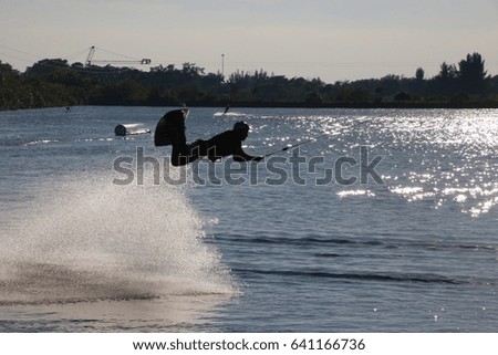 Wake Boarder in Mid-Air from Half Somersalt Leaving Plume of Spray Being Pulled Across Lake in Silhouette against Sunlit Water Sparkles Late in the Afternoon at Quiet Waters Park