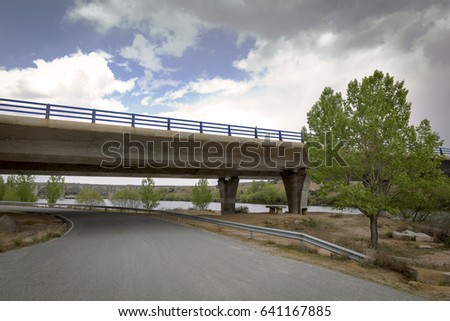 Road passing under a bridge of a motorway next to a dam and an old railway bridge
