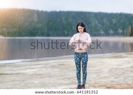 Young woman peacful meditating by the lake. Fitness girl doing yoga at morning sunrise in nature background