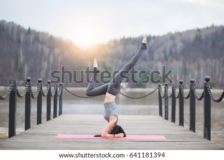 Young girl doing yoga Handstand pose or fitness exercise outdoor in nature with beautiful lake and mountains landscape at morning sunrise, Namaste pose. Meditation and Relax concept