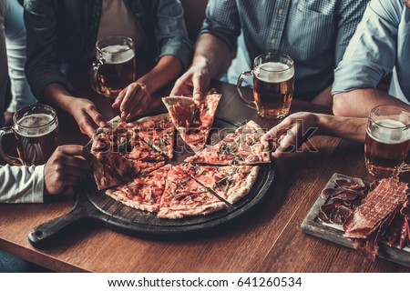 Close-up of handsome young friends drinks beer and eating pizza at pub.