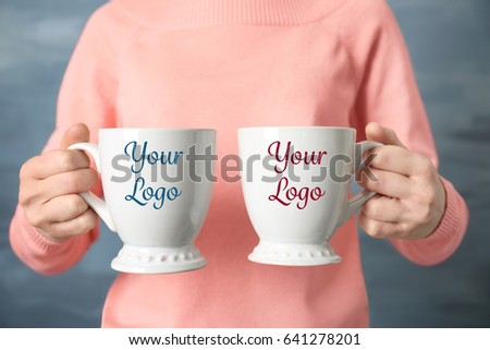 Woman holding cups with space for logo on blurred background