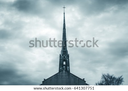 Church steel brass spire. Church building roof with spire and holy cross. Cloudy moody sky background. Minimal architecture design and detail. Exterior design and detail. Abstract architecture. 