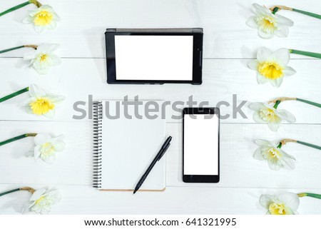 Top view on table with narcissus, empty diary, pencil, tablet and phone, free space. Yellow narcissus on white wooden background. Blank card flat lay