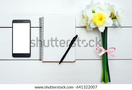 Yellow bouquet of narcissus on white wooden background. Blank card flat lay. Top view on table with narcissus, empty diary, pencil and phone, free space
