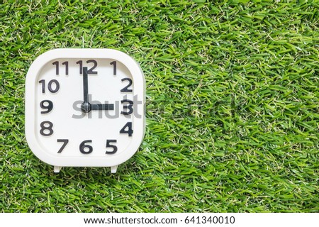 Closeup white clock for decorate in 3 o'clock on green artificial grass floor textured background with copy space