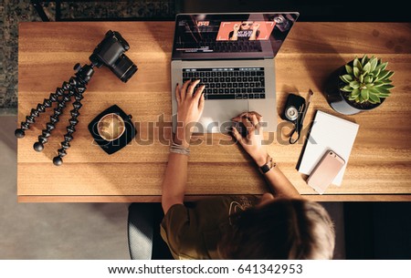 Top view of female vlogger editing video on laptop. Young woman working on computer with coffee and cameras on table. Royalty-Free Stock Photo #641342953