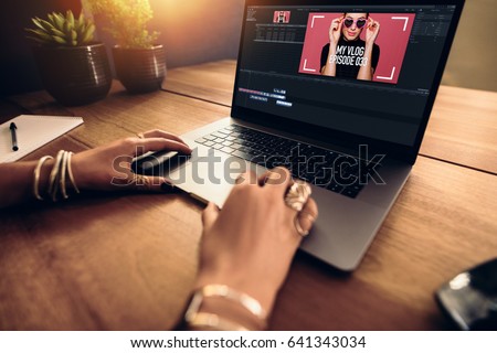 Woman editing video on laptop computer for her vlog. Woman wearing fashionable rings working on laptop on a wooden table.