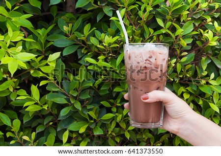 Hand woman holding the glass iced cocoa on green nature background