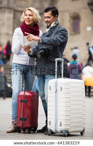 Happy smiling mature couple with suitcases, camera and map outdoors
