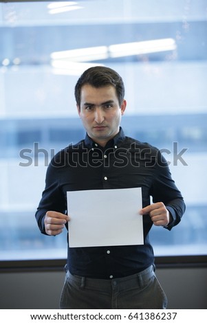 Serious adult office employee showing clear sheet of paper, Vertical indoors shot