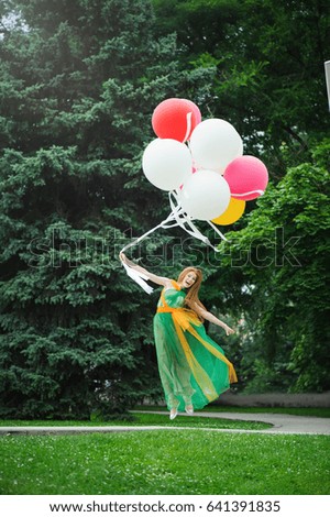 young woman in green dress with balloons jumping on the green background.