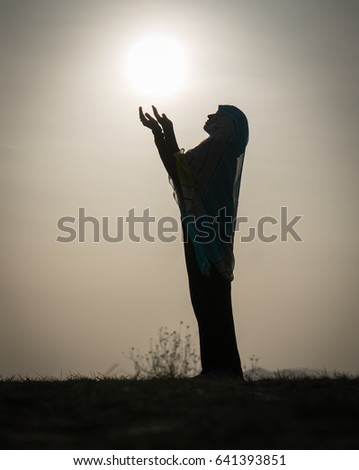 Silhouette Muslim Arabic woman praying with her hands up