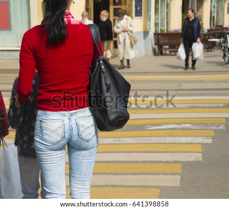 people walking in the street, Busy city street people on white and yellow zebra crossing. Focus on ass in blue stylish jeans and red sweater. mother with daughter and big black leather handbag