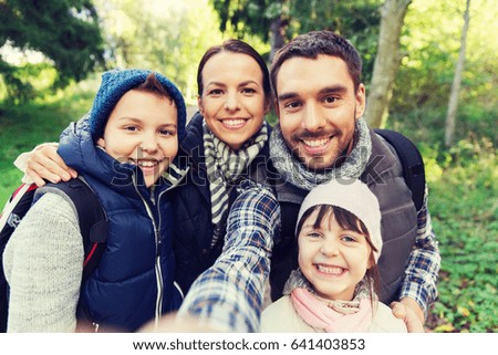technology, travel, tourism, hike and people concept - happy family with backpacks taking selfie and hiking