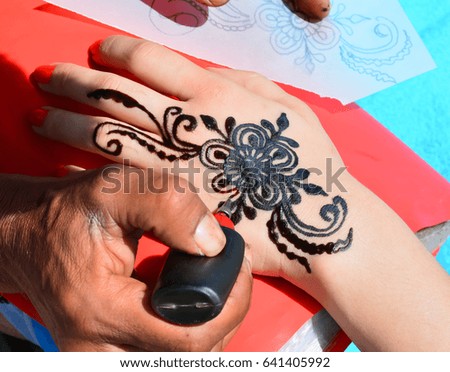 Artist applying henna tattoo on women hands