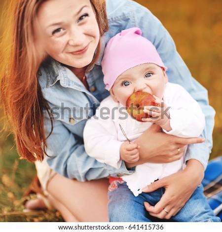 colorful picture of the young happy mom having fun with her daughter holding big juicy apple in the meadow