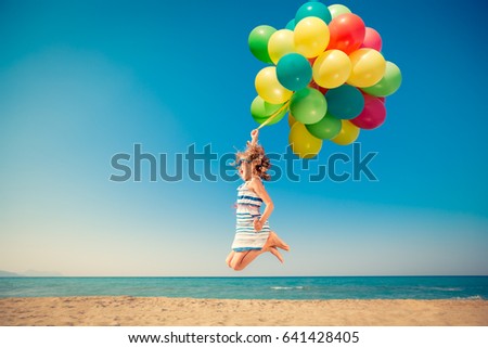 Happy child jumping with colorful balloons on sandy beach. Portrait of funny girl against blue sea and sky background. Active kid having fun on summer vacation. Freedom and imagination concept Royalty-Free Stock Photo #641428405