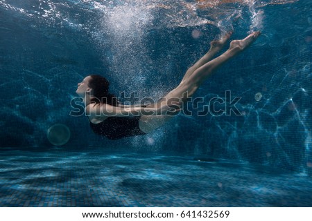 Woman floats under water in the pool, around her vials of air and spot of light. Royalty-Free Stock Photo #641432569