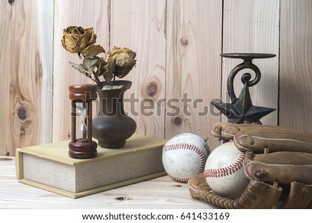 Baseball and glove on wooden table with book and candle holder. Rose withered and hourglass