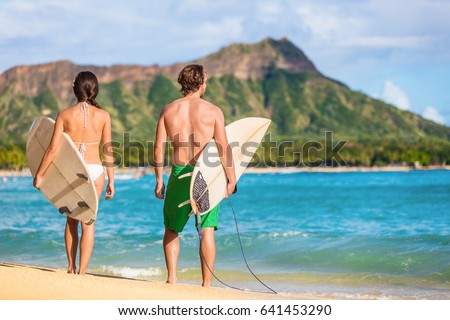 Hawaii surfers people relaxing on waikiki beach with surfboards looking at waves in Honolulu, Hawaii. Healthy active lifestyle fitness couple at sunset with diamond head mountain in the background.