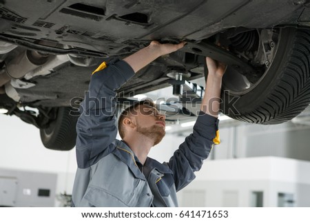 Professional auto mechanic working on the undercarriage of a car diligence attention inspection examination annual checkup safety insurance professionalism occupation transportation vehicle concept Royalty-Free Stock Photo #641471653