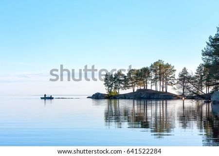 View on Onega Lake with fishers in boat and trees on cape reflecting in calm water at midnight sun. Karelia Republic, Russia.
