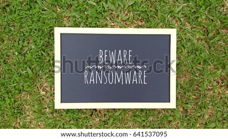 conceptual image with word HAPPY BEWARE RANSOMWARE on Chalkboard at beautiful green background.

