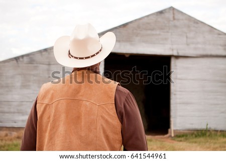 Rear view of a cowboy looking at an empty barn.