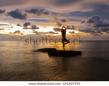 Long Exposure Photography of woman practices yoga on the rock, beach at sunset (yoga, meditation, peace)