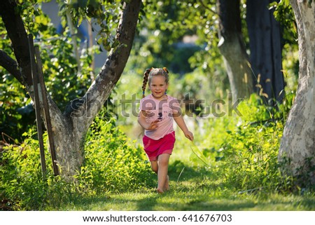Cute little girl running barefoot with a scoop-net on a sunny meadow in the garden