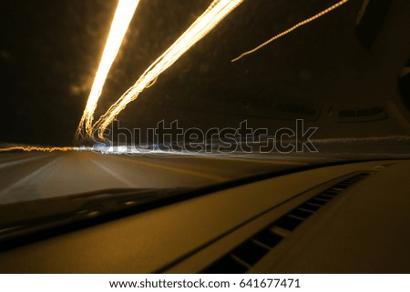 Street lights in speeding car in night time, light motion with slow speed shutter view from inside front of car.