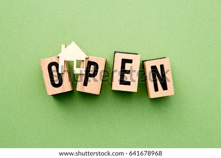 Open House - wooden block letters with home icon on green background
