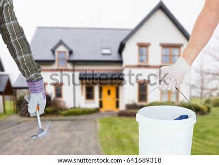Digital composite of hand with hammer and hand with a cube in front of a real house