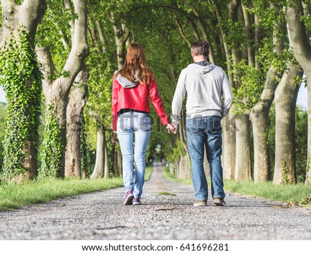 a man and a woman joining hands on a mysterious road with trees along it resembling a tunnel through sunlit woodland
